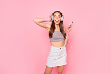 Obraz na płótnie Canvas Portrait of lovely youth with her eyes closed holding modern technology wearing white skirt denim jeans grey tank-top isolated over pink background