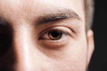 close up view of adult man brown eye with eyelashes and eyebrow looking at camera isolated on black