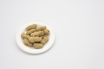 A plate of shelled peanuts quietly placed on a white background left side top view