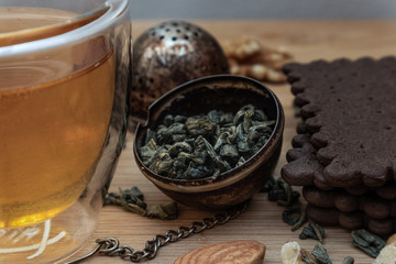 Fototapeta na wymiar Green tea leaves in metal tea bag and cup of tea with walnuts and biscuits on wooden plank