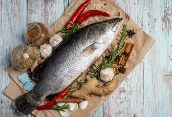 Fresh Raw Sea Bass on wooden table surrounded by fresh ingredients and spices.