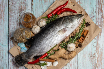 Fresh Raw Sea Bass on wooden table surrounded by fresh ingredients and spices.