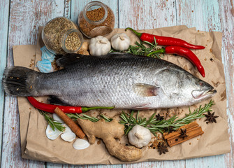 Fresh Raw Sea Bass on wooden table surrounded by fresh ingredients and spices.
