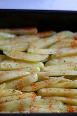 Potato slices drizzled with olive oil, basil and smoked paprika, ready for oven. Selective focus.