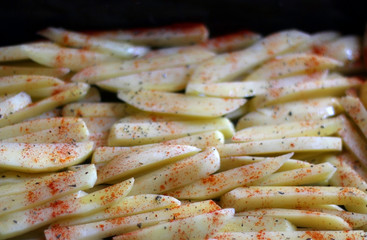 Potato slices drizzled with olive oil, basil and smoked paprika, ready for oven. Selective focus.