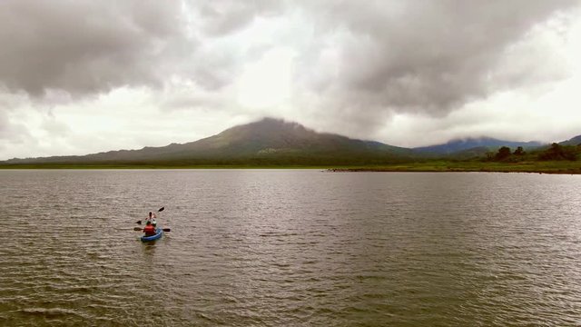 Kayakers paddle towards Arenal Volcano on Lake Arenal Costa Rica, aerial tracking shot from a drone