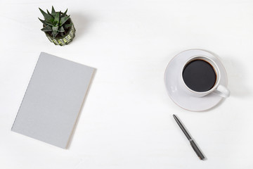 Top view of white working table with closed copybook, white cup of coffee, pen and green succulent plant. Work space for school or office. Copy space. Flat lay.