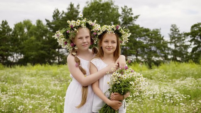 Couple Girls Laugh Friends Hug Flowers Meadow. Happy Caucasian Children Embrace Floral Wreath Pose Picture. Cute Kids Enjoy Nature Hold Wildflowers Bouquet Free Time Leisure Concept