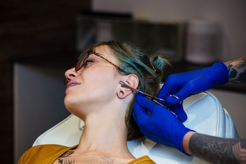 Young Woman getting her ear pierced. Man showing a process of piercing with steril medical...