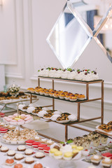 Beautifully decorated catering banquet table with burgers, profiteroles, salads and cold snacks. Variety of tasty delicious snacks on the table