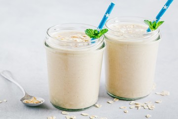 Banana oats smoothie or milkshake in glass mason jars on a stone background