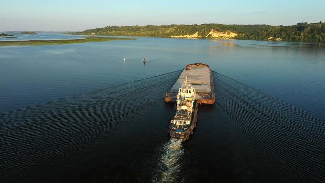 Aerial video river pusher boat transporting barge with dry cargo in middle of summer river, Central Europe