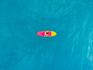 Woman relaxing on stand up paddle board on a quiet blue sea. Aerial view