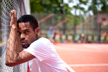 Black basketball player holding the chain link fence with hands