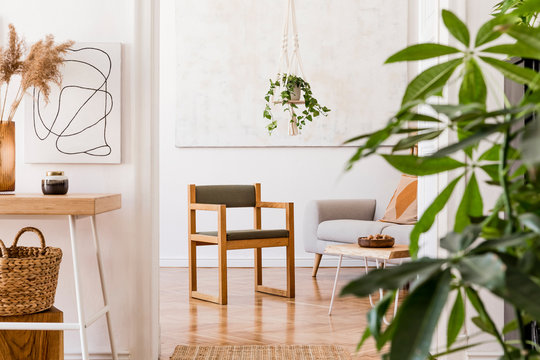 The nice boho open space interior at cozy apartment with design gray sofa, wooden desk, armchair, coffee table, plants, and elegant accessories. Mock up poster on the white wall. Stylish home decor.