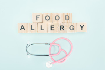 top view of wooden blocks with food allergy lettering near stethoscope isolated on blue