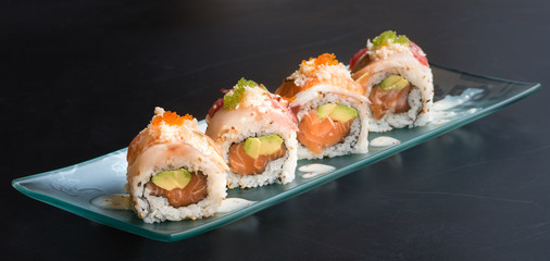 Special Uramaki, rice roll stuffed with salmon avocado, covered with sashimi of bluefin tuna and sea bass, seasoned with cheese sauce, black background