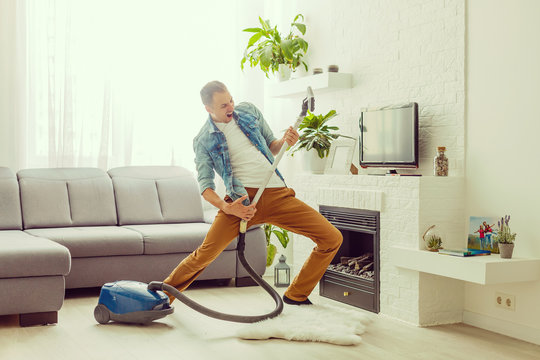 Young Man Having Fun Cleaning House With Vacuum Cleaner Dancing Like Guitarist