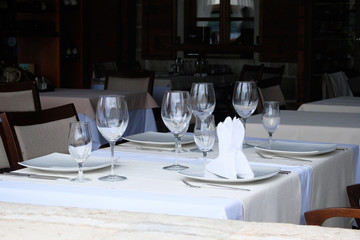 Glasses set in restaurant. Part of interior. Glasses, fork, knife served for dinner in restaurant with cozy interior.
