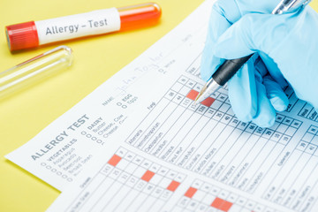cropped view of woman in latex glove filling in papers near test tubes with allergy test lettering isolated on yellow