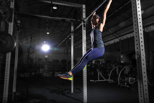An athletic and beautiful woman is doing a fitness workout in a gym.The muscular female athlete is hanging in the l sit position on the horizontal bar. Sport in the gym.