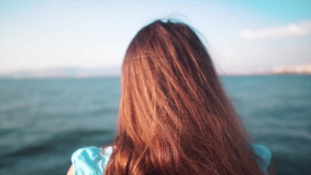 Thoughtful teenager girl is watching sea, trying to relaxing. Back of worried young girl is alone, red hair. Depression, unhappy women concept.