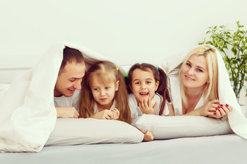 Children and parents rest in the morning in bed. They indulge, hug. Twins. daughters.