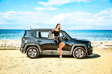 Fototapeta na wymiar A girl on a black car on a sandy beach and blue ocean view.
