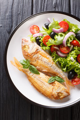 Tasty fried pink dorado or gilt-head bream fish with vegetable salad close-up on a plate. Vertical top view