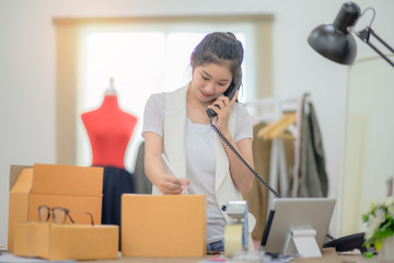woman tailor made packing goods into boxes containers, ready to delivery to customer under address inform on calls of the phone and online device