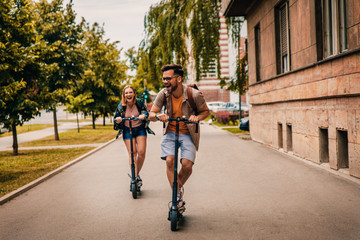 Young couple on vacation having fun driving electric scooter through the city.