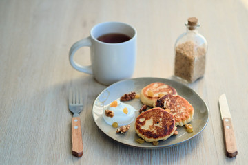 Close-up of homemade cheese pancakes syrniki with sour cream and cup of tea