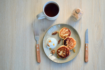 Top view of homemade cheese pancakes syrniki with sour cream and cup of tea
