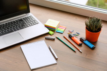 An open notebook for notes, pencils, markers, a pen, a pot with cactus, a notebook and paper clips on a wooden background (office desk). - Powered by Adobe