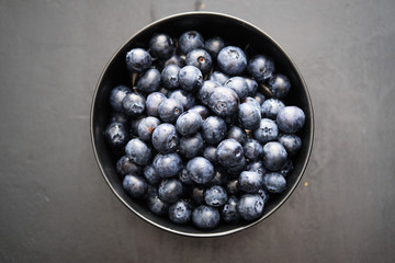Top view of freshly picked blueberries in black bowl on dark background