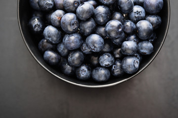 Top view of freshly picked blueberries in black bowl on dark background