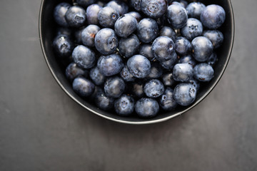 Top view of freshly picked blueberries in black bowl on dark background