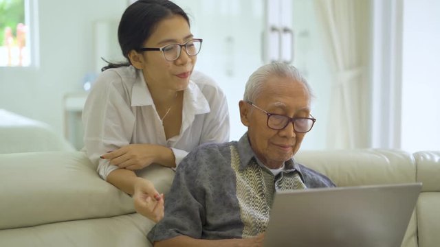 Elderly man using a laptop computer with his daughter on the sofa in living room at home. Shot in 4k resolution