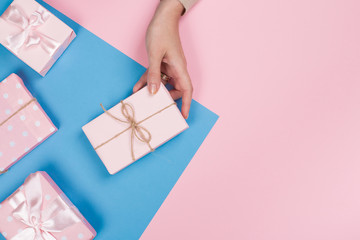 Womans hands holding gift or present box on pink pastel table top view. Flat lay composition for birthday or New Year.