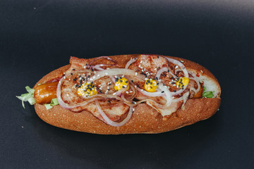 Big hotdog with sausage tomatoes, mustard and salad isolated on black background.