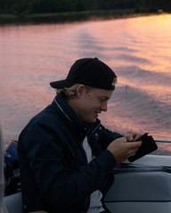Guy sitting on a boat in the sunset looking at his phone.