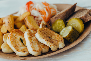Tasty grilled fish with fried potatoes, cucumber, cabbage and woods in a paper plate on a wooden table. takeaway street food