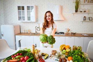 Young happy woman holding broccoli and cabbage in the beautiful kitchen with green fresh ingredients indoors. Healthy food and Dieting concept. Loosing Weight