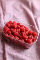 Fresh raspberries in a container. Selective focus, pink background.