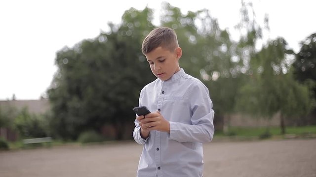 Handsome boy use phone outside. Little boy on the back yard of school
