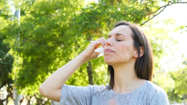 Adult woman suffering heat stroke sweating and drying face with a wipe in a park