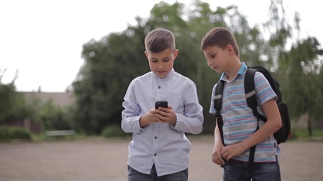 Two boys plays online games after school classes. Young boys smile and use phone