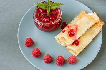 Glass jar with raspberry jam with homemade pancakes, fresh berries and mint on a gray background.Copy space
