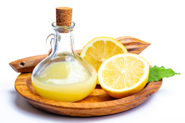 Fresh lemon juice made from ripe yellow Sicilian lemons used for cooking in glass bottle on olive wood plate