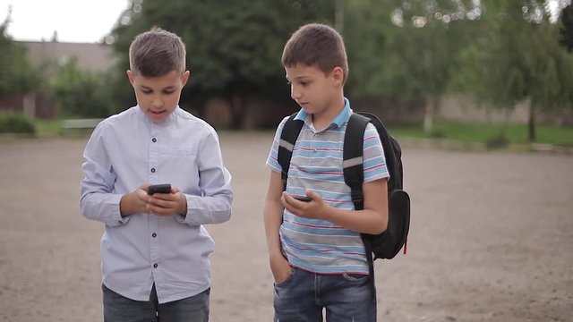 Two boys plays online games after school classes. Young boys smile and use phone